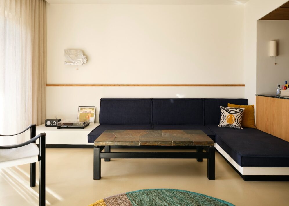 A minimalist living room with a navy blue L-shaped sofa, yellow and patterned cushions, a stone coffee table, and a vintage record player on a shelf.