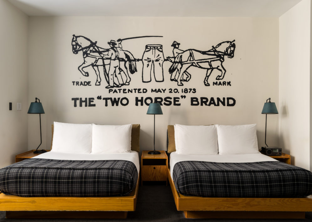 Two beds are flanked on all sides by tall side lamps, and original custom art is painted on the wall above the beds