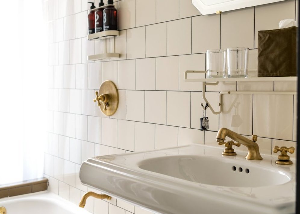 An elegant white tiled bathroom features golden faucets and handles