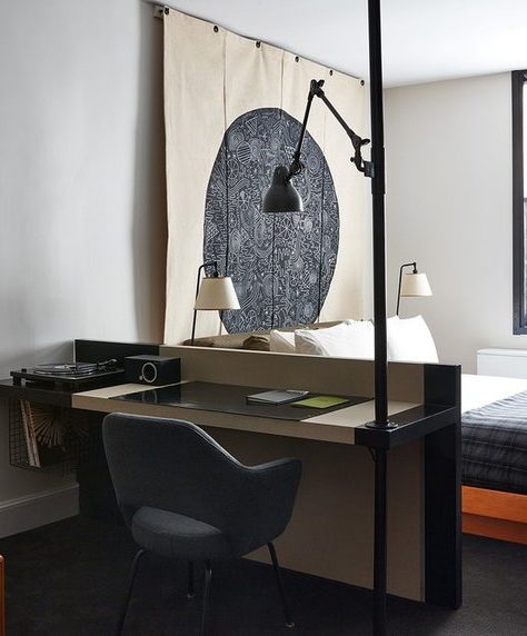 A modern room features a desk for work with a tall light overlooking the desk and a window for additional natural light