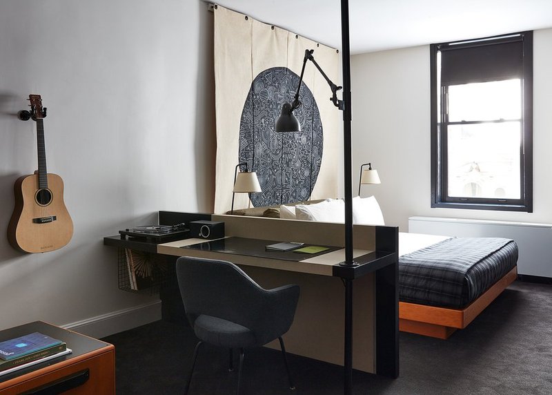 A modern room features a desk for work with a tall light overlooking the desk and a window for additional natural light