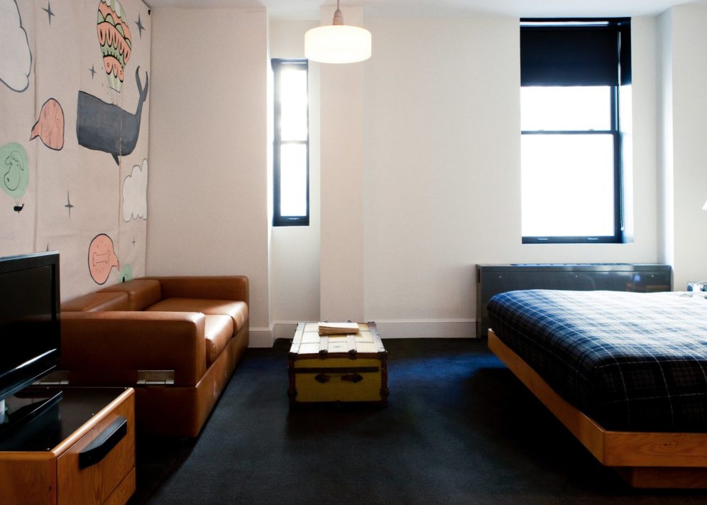 A room with dark carpets features two windows and a brown leather sofa