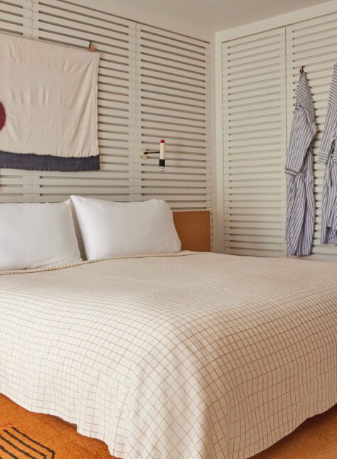 A bed with plaid bedding is drenched in natural light and an ornate brown rug adorns the floor