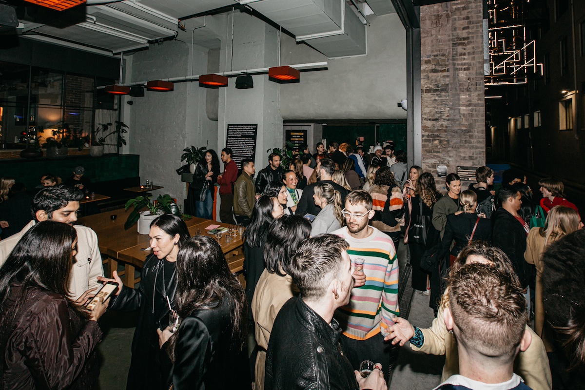 A large group of people socialize at an indoor event space with tables and exposed brick walls.