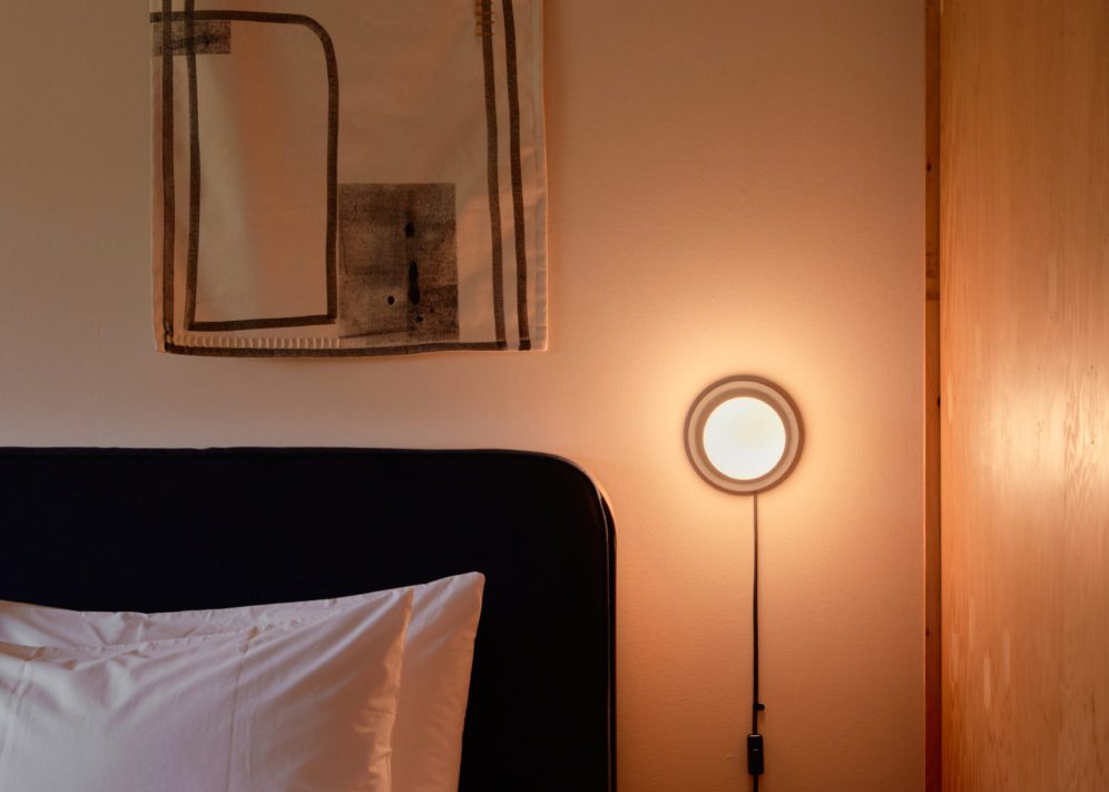 A modern mounted wall light sits next to a bed, providing an opportunity for late night reading