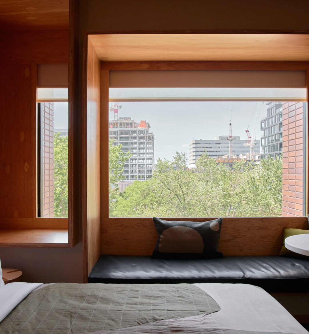 A wood paneled room features a black leather seating area under a window featuring greenery